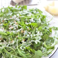 a plate of arugula with pine nuts, lemon dressing, red chili flakes and pecorino