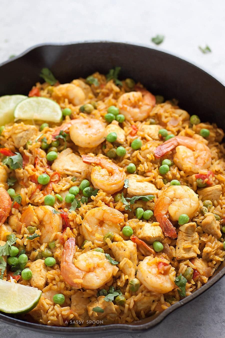 Chicken and shrimp paella cooking with brown rice, peas, and lime slices
