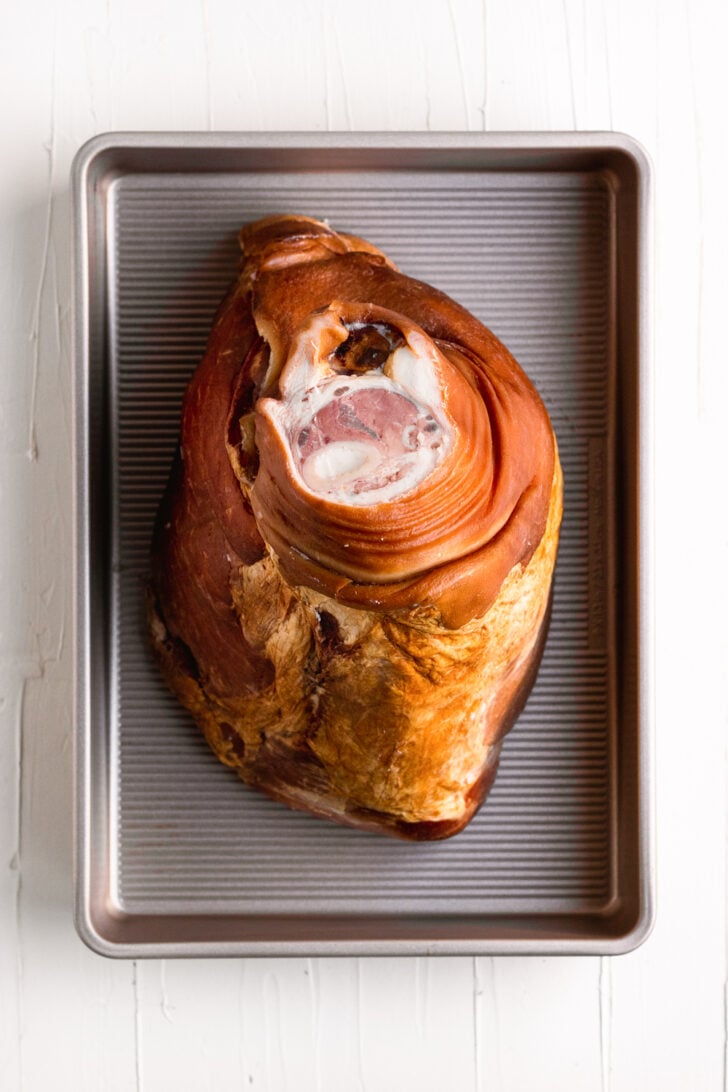 Slow-roasted pork shank on baking sheet, ready for cooking, savory meat cut, crispy skin, culinary delight.
