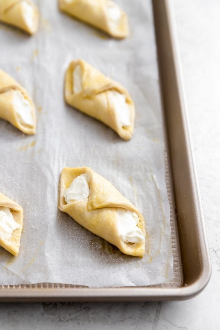 Unbaked pastelitos de queso on a parchment-lined baking sheet.