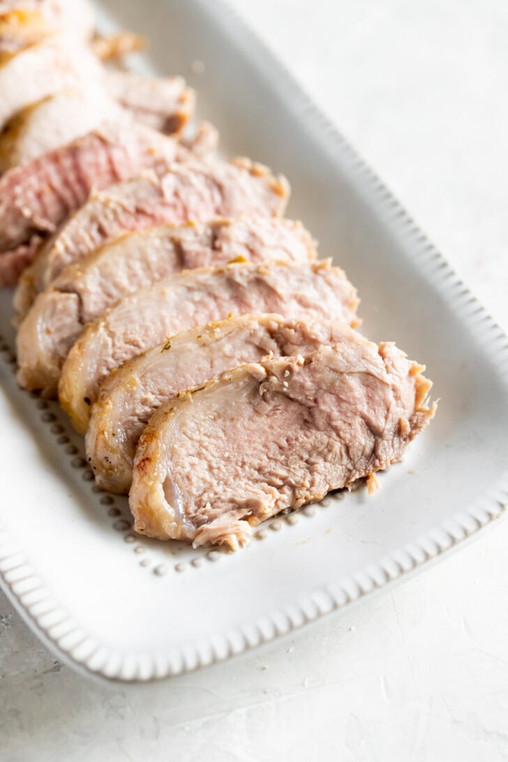 Slices of cooked pork tenderloin for a Cuban sandwich arranged on a white rectangular platter.