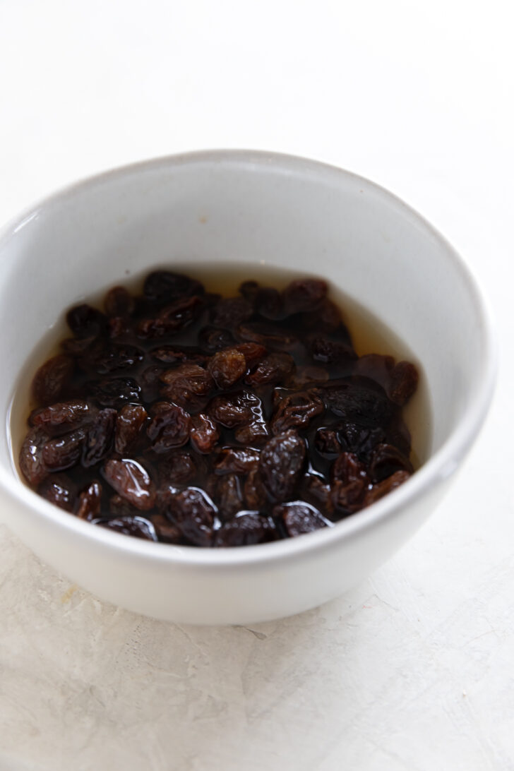 Dried raisins soaking in water in a white bowl for baking or cooking recipes.