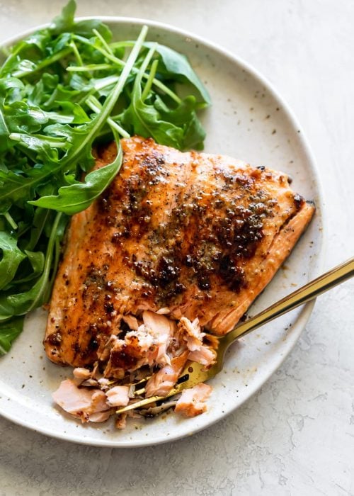 honey mustard salmon broken in pieces on a speckled plate with arugula salad