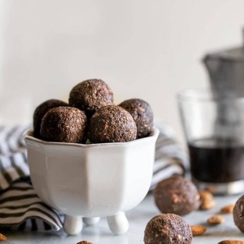 balls made with almonds, dates, chia seeds, coffee and cocoa powder in a white dish on a marble slab