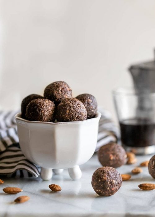 balls made with almonds, dates, chia seeds, coffee and cocoa powder in a white dish on a marble slab