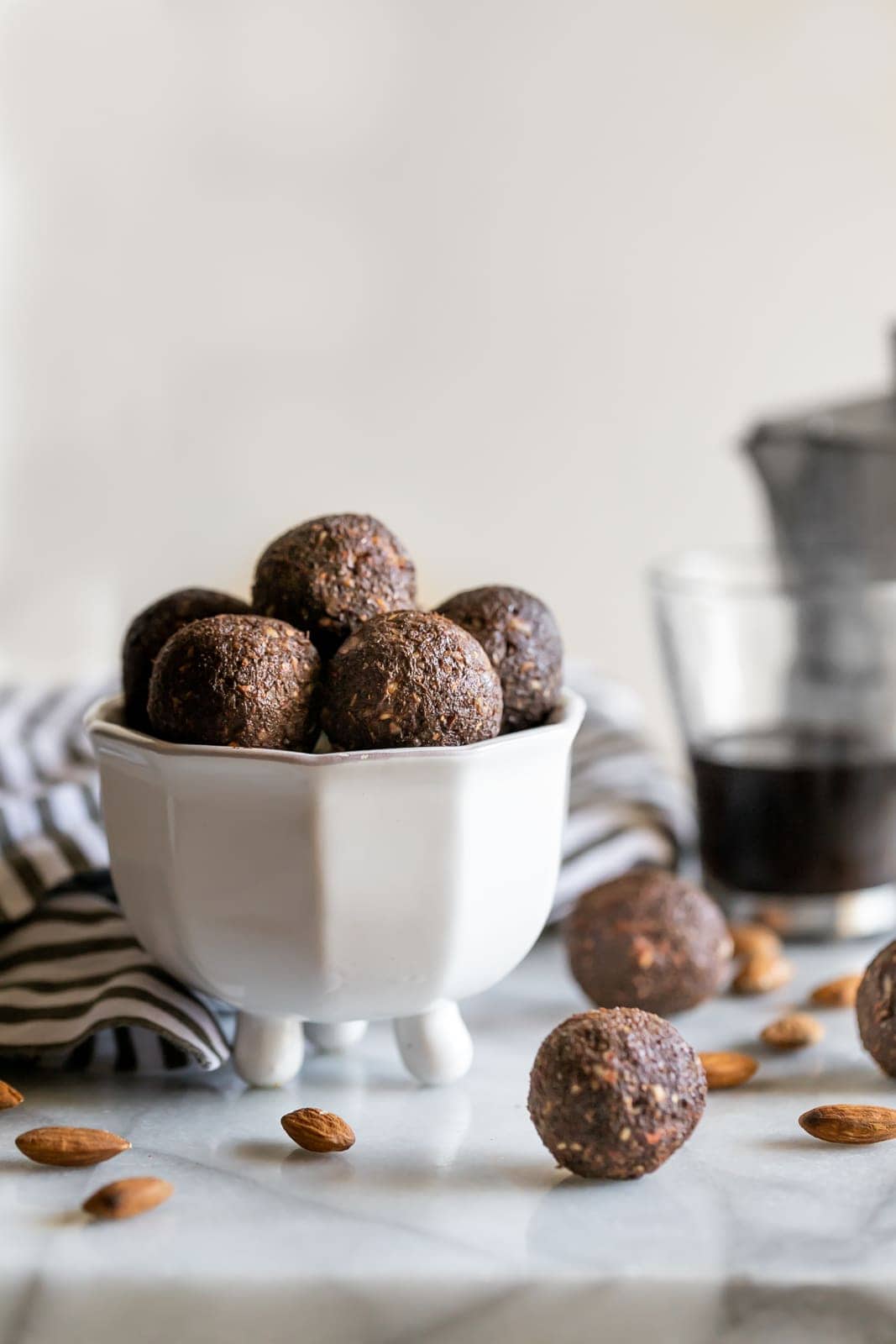 balls made with almonds, dates, chia seeds, coffee and cocoa powder in a white dish on a marble slab