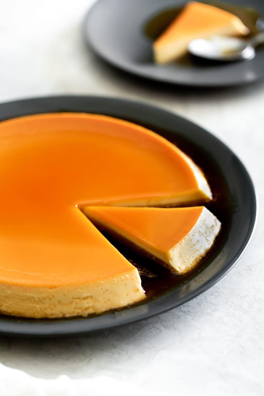 flan de queso with a slice taken out on a black plate