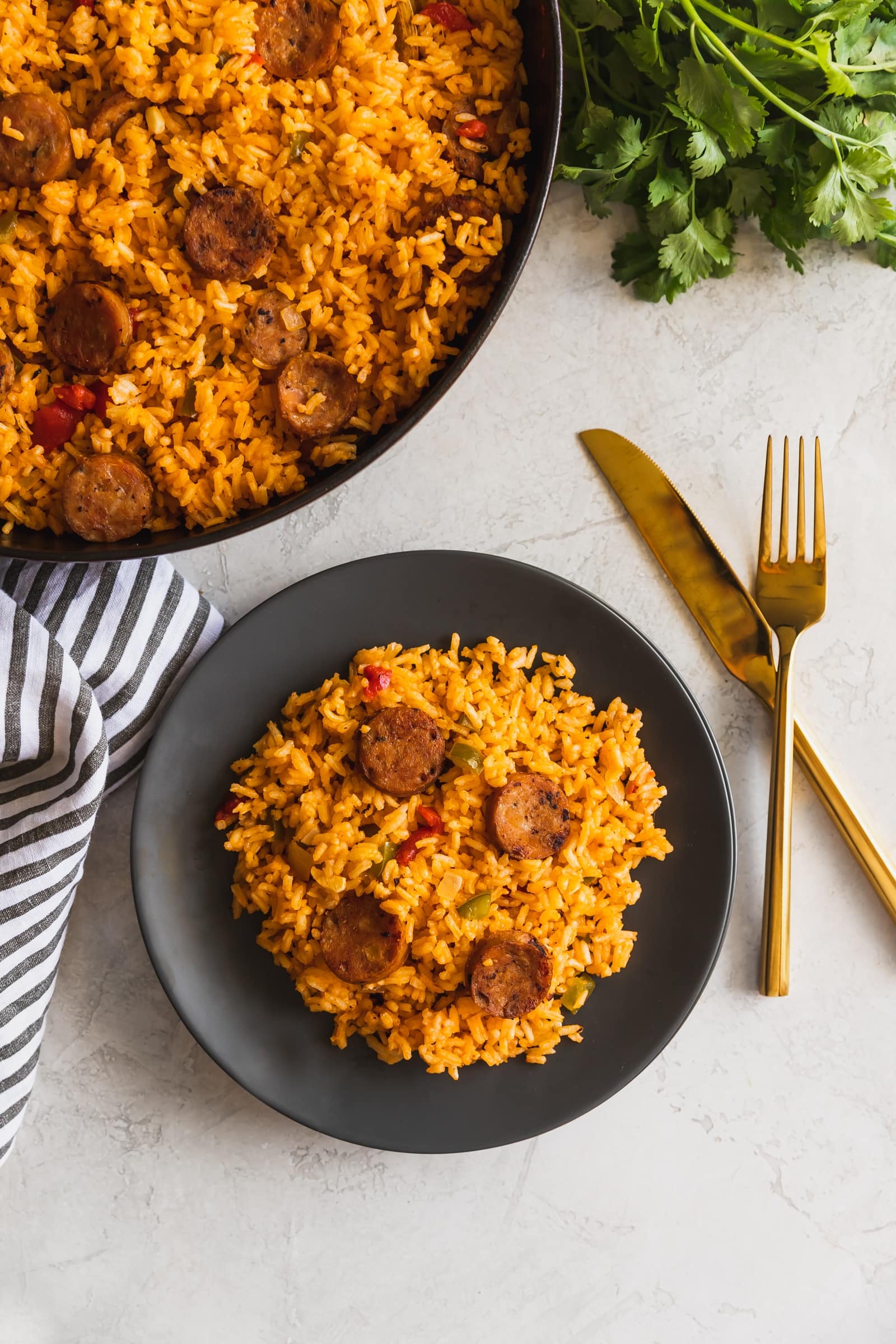 Cuban arroz con salchichas served on a gray plate with gold utensils on a white table