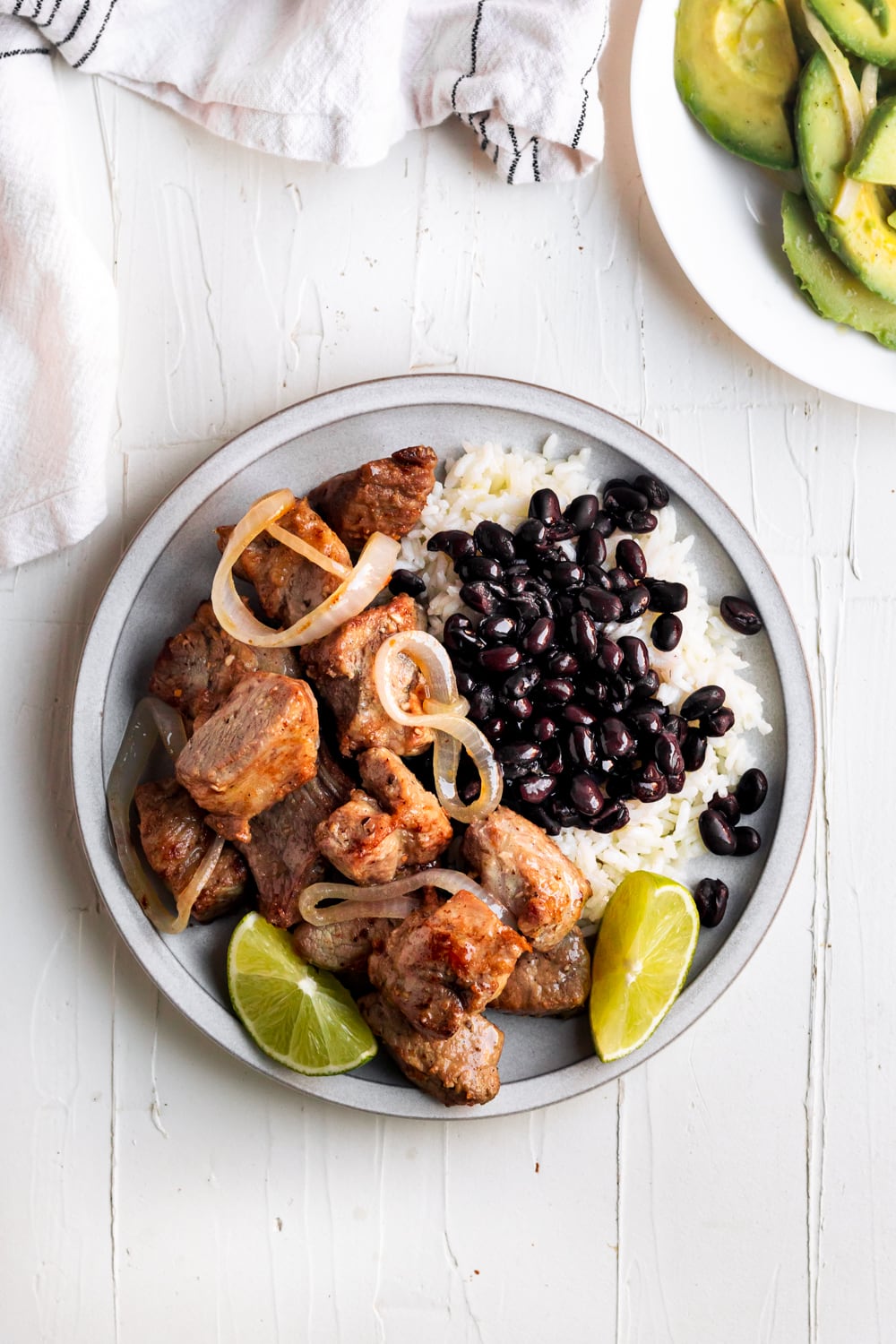 masitas de puerco with onions on a plate served with black beans & rice, and lime wedges
