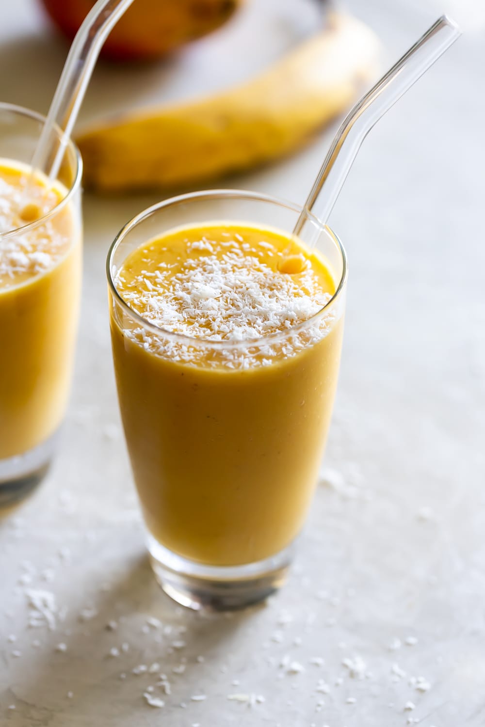 mango shake in a large glass with shredded coconut flakes on top