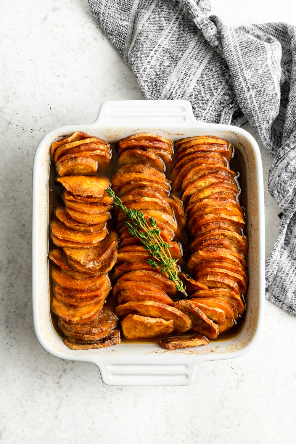 baked sliced sweet potatoes out of the oven with thyme sprigs