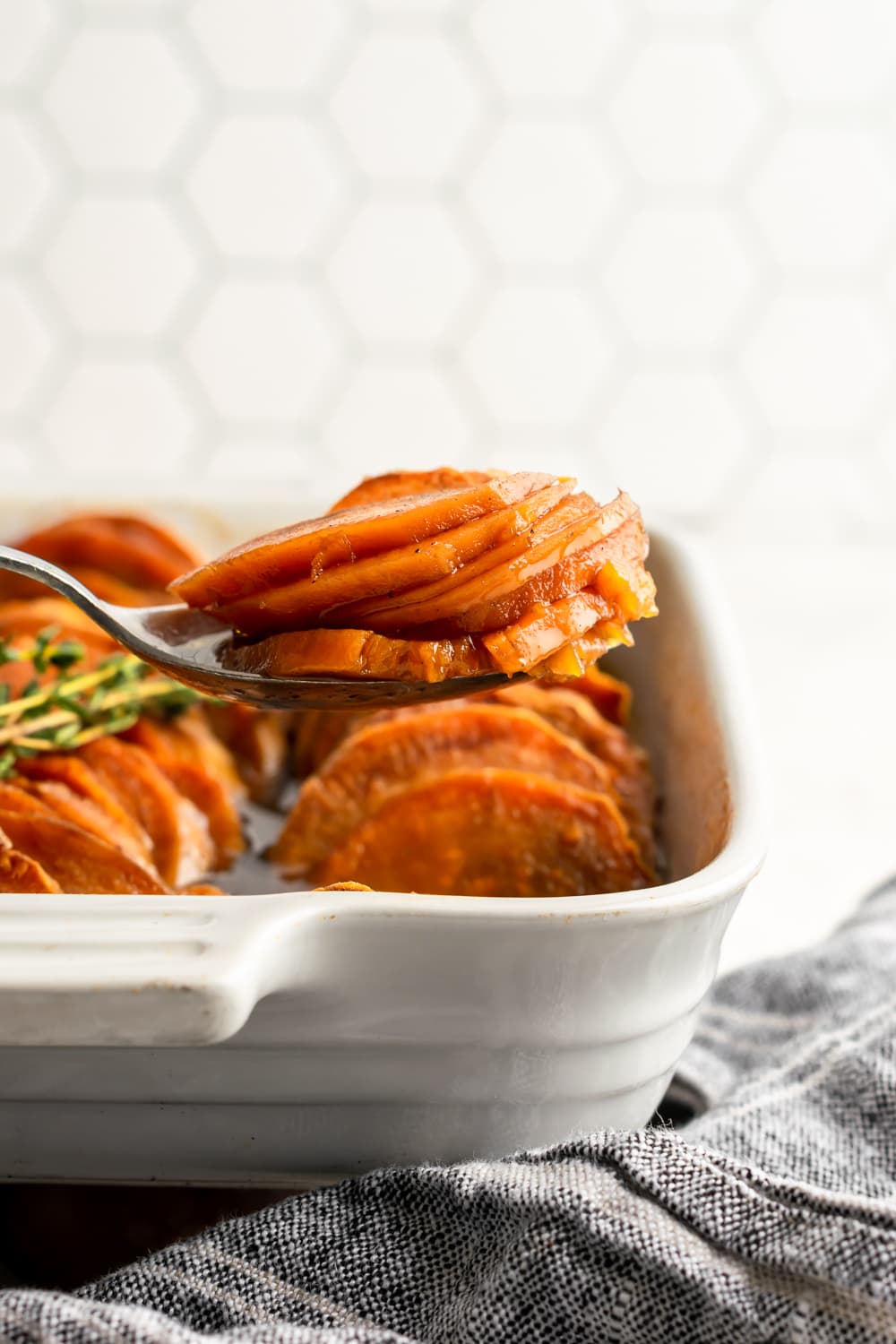 spoonful of candied sweet potatoes in a white baking dish on a white background