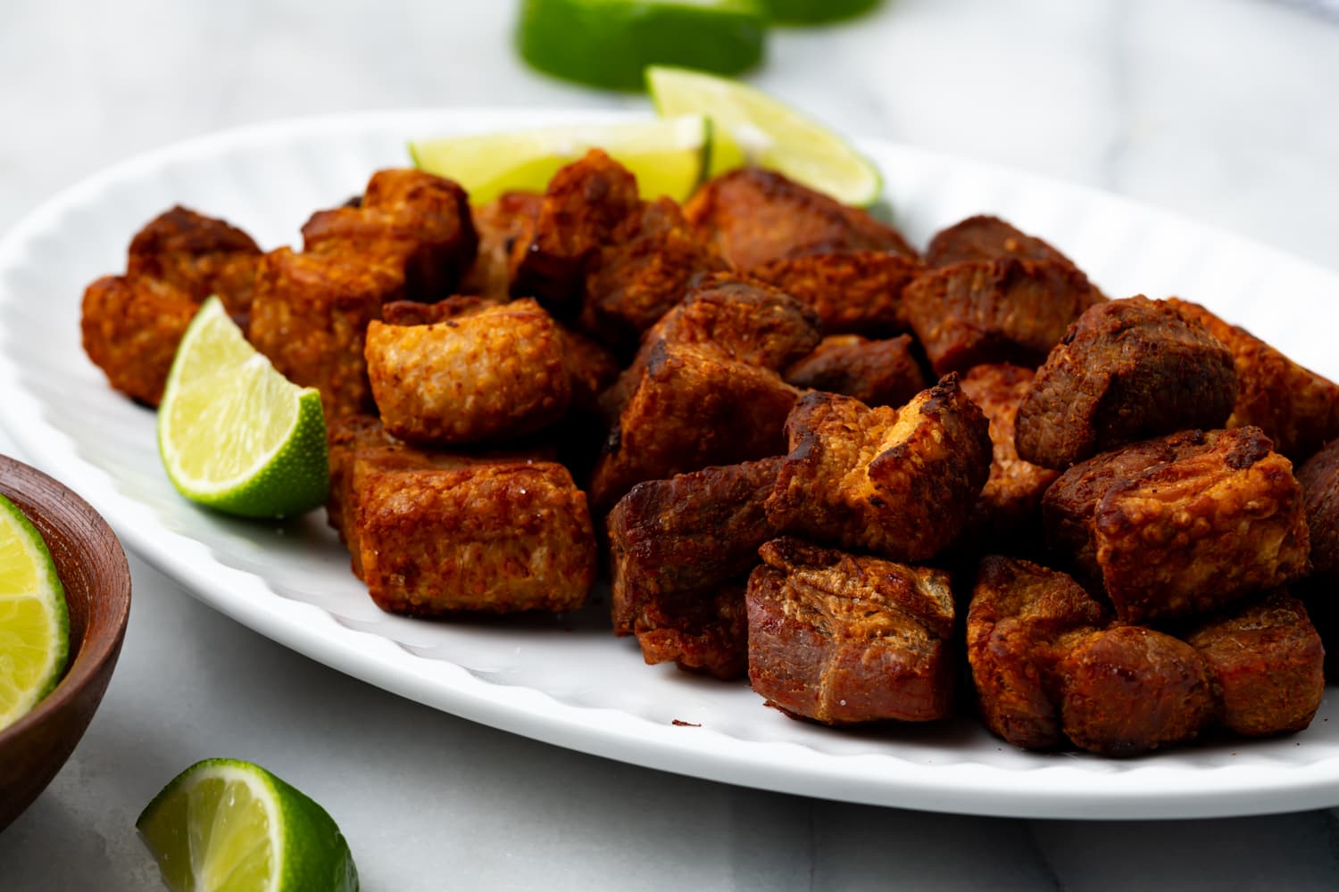 chicharrones de puerco on a white platter with lime slices garnishing.