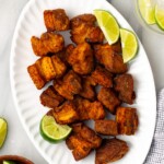 An overhead shot of chicharrones de puerco on a white platter with lime slices on the side on a white counter.