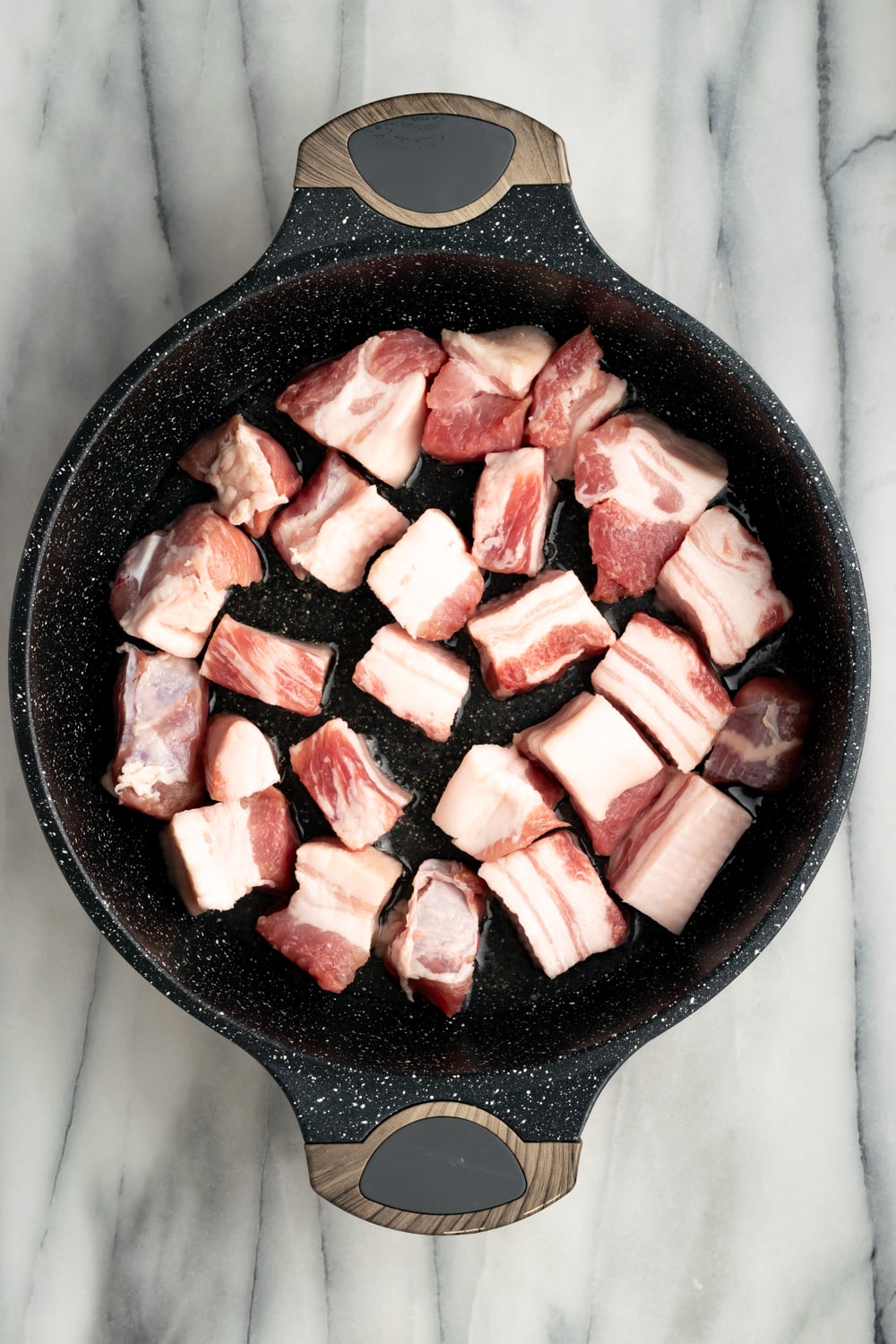 Uncooked pork belly pieces in a cast iron pan to make chicharrones de puerco on a marble countertop