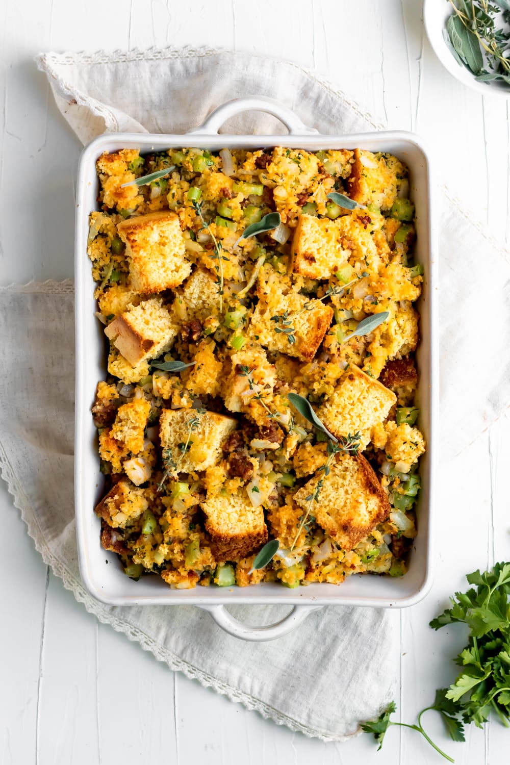 chorizo cornbread stuffing with fresh herbs in a baking dish on a white surface