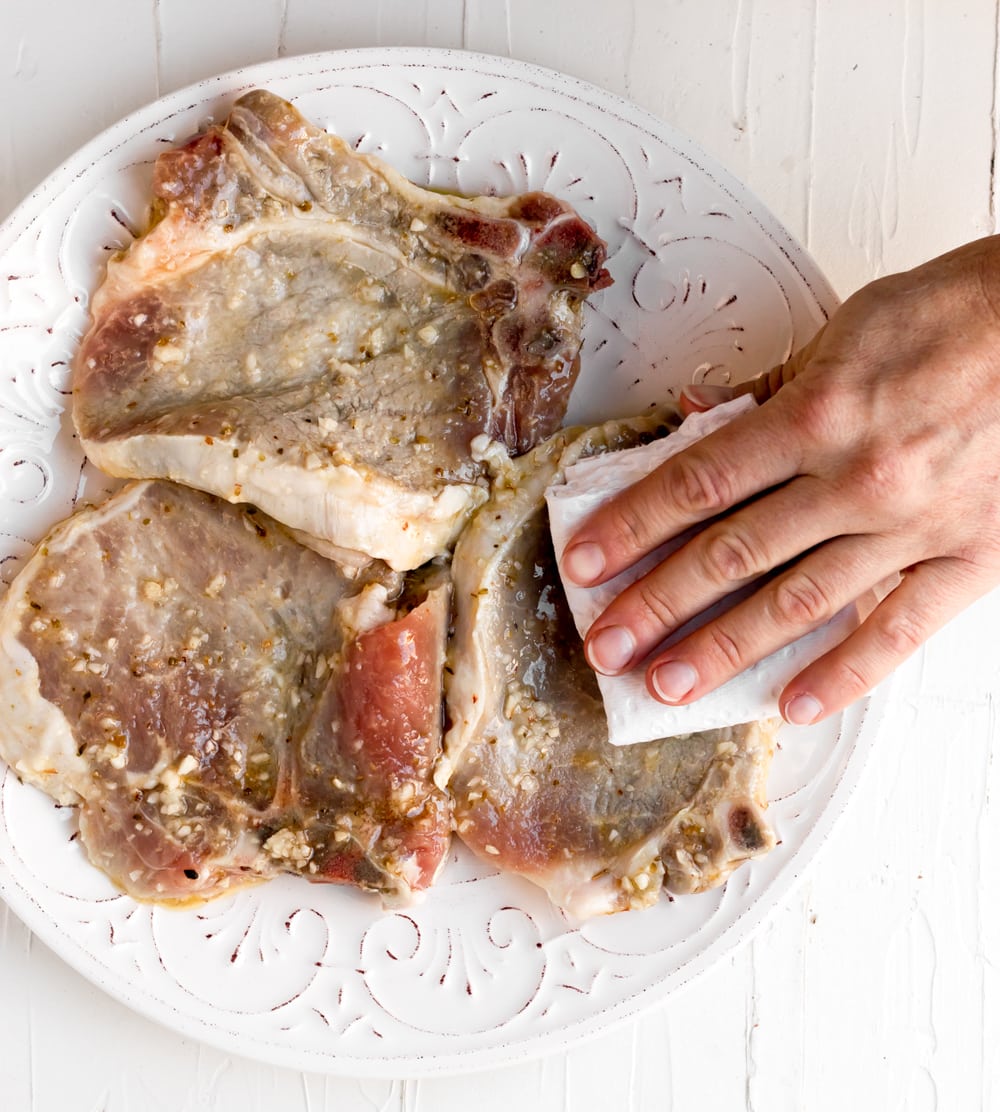 Marinated chuletas de puerco being patted dry with a paper towel