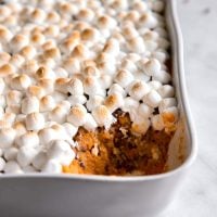 mashed sweet potato with toasted marshmallows on top in a casserole dish with a spoonful missing
