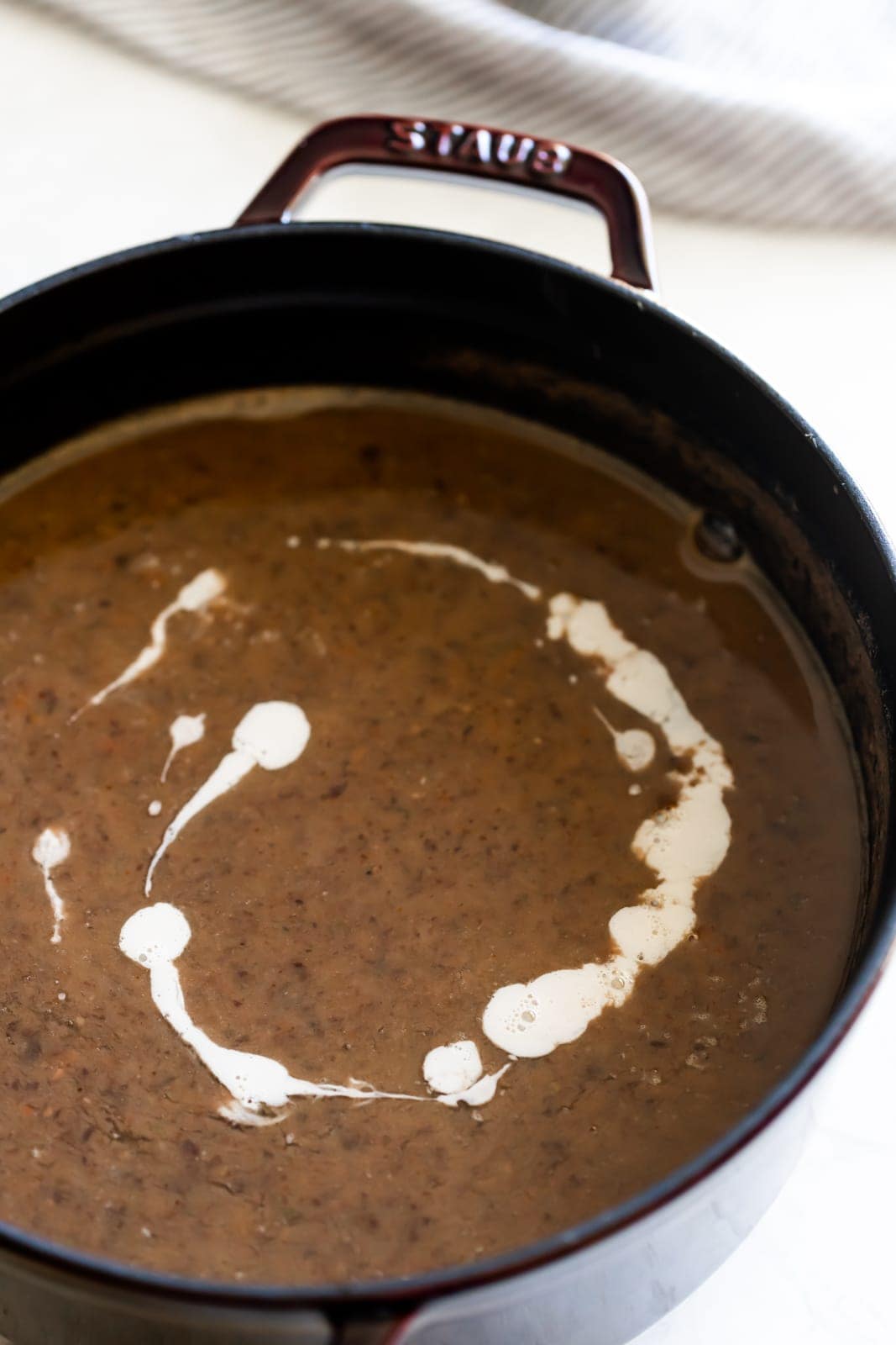 dutch oven with cooked black bean soup and a drizzle of cream