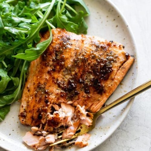 honey mustard salmon broken in pieces on a speckled plate with arugula salad