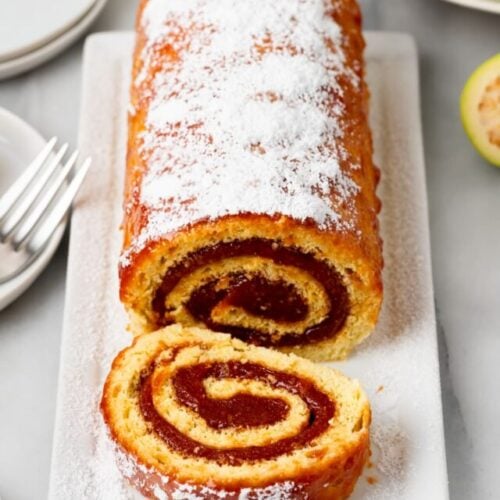 A brazo gutano (guava swiss roll) on a white platter that has a slice cut off and still sitting on the platter