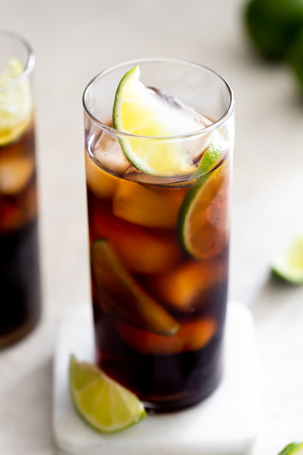 tall glass of cuba libre drink with ice and lime wedges