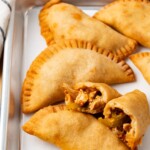 Chicken Empanadas on a parchment lined baking sheet one empanada is broken in half