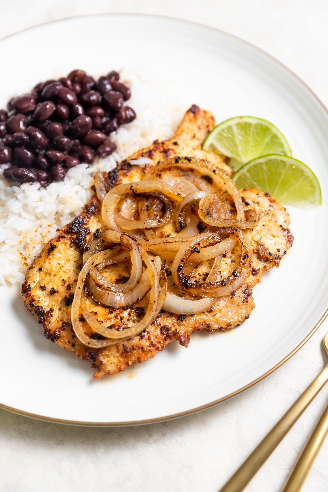 pollo a la plancha with sauteed onions and rice and beans on a white plate