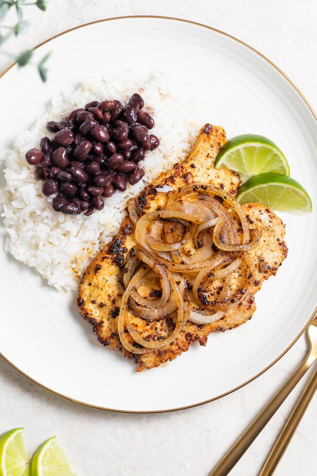griddled chicken breast with sauteed onions on top served with white rice with Cuban black beans on a white plate
