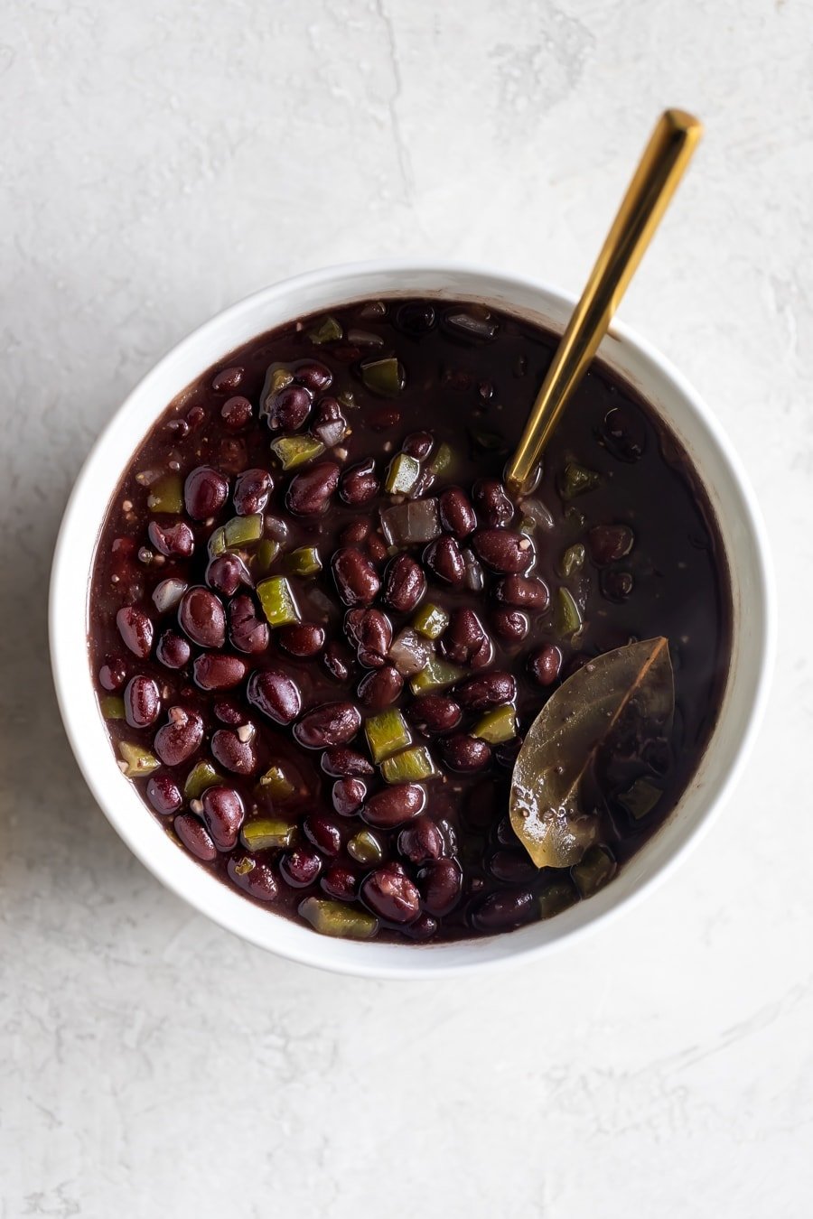 white bowl of frijoles negros (Cuban black beans) with a gold spoon