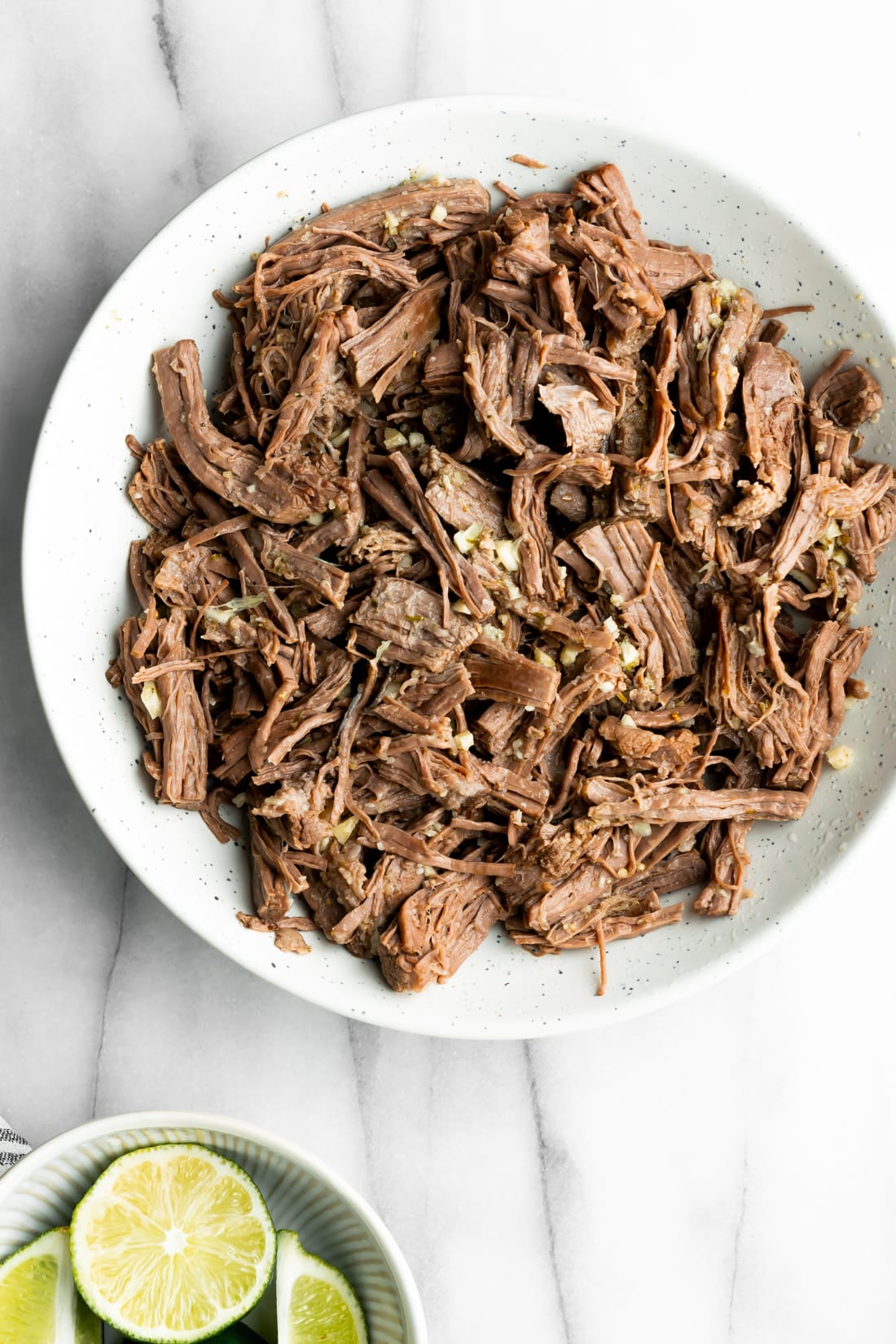shredded beef on a white plate with minced garlic before pan frying