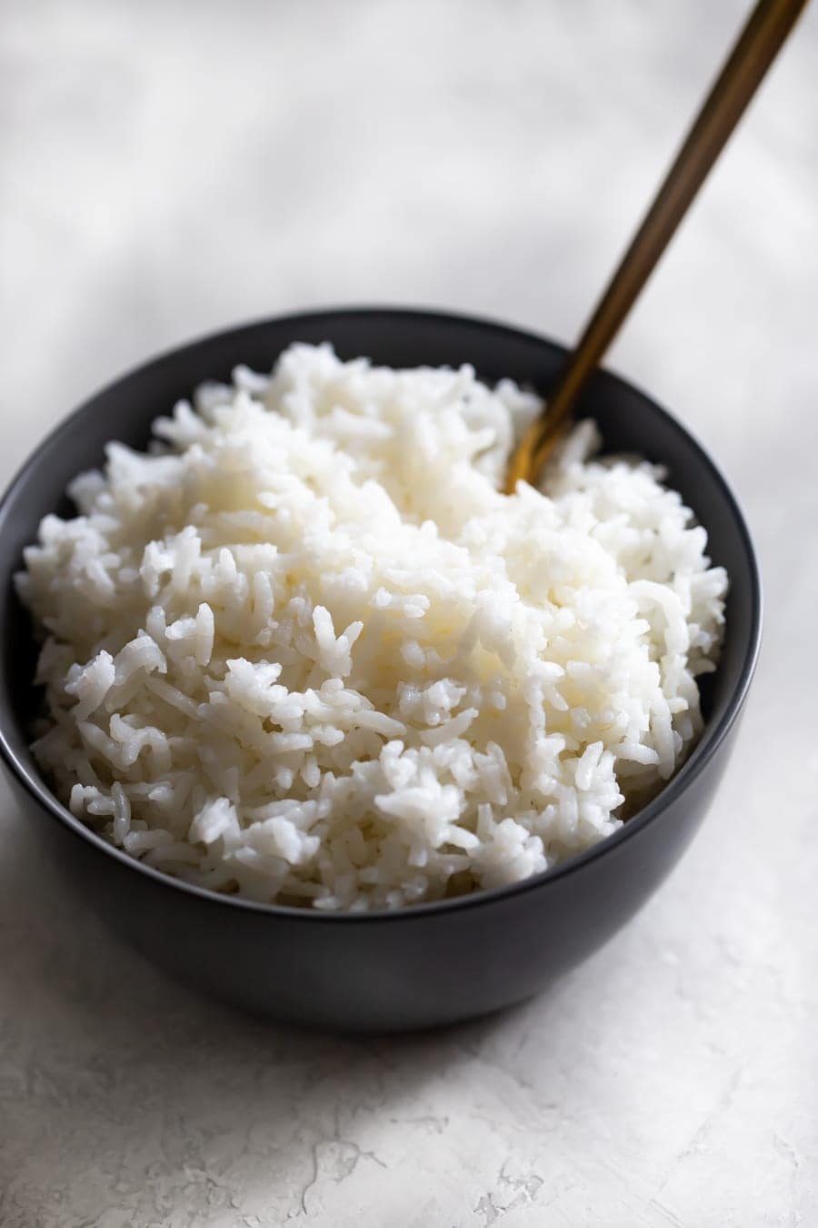 cooked white rice in a gray bowl with a gold spoon