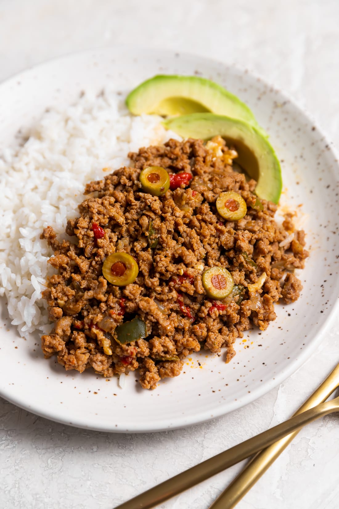 easy turkey picadillo on a white plate with sliced avocados and white rice