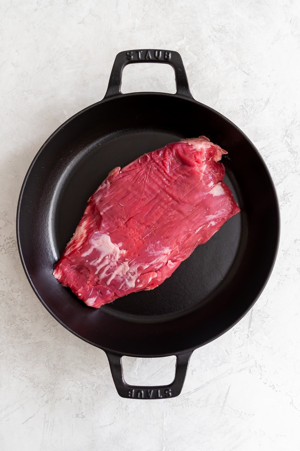 raw flank steak on a braiser before cooking and shredding