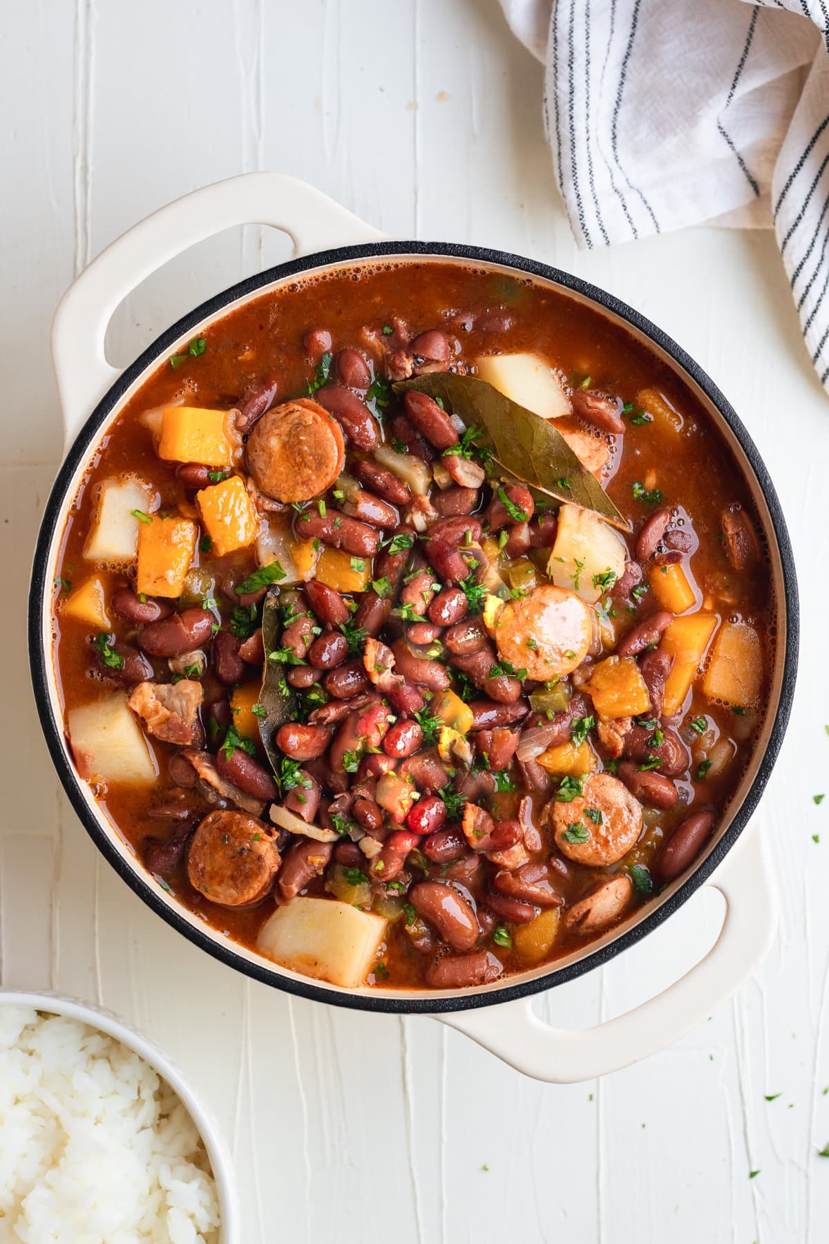 Cuban frijoles colorados in a Dutch oven with red kidney beans, squash, ham, bacon, chorizo, sofrito, and spices.