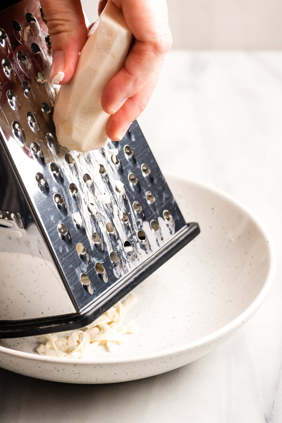 grating the peeled malanga with a box grater onto a white plate