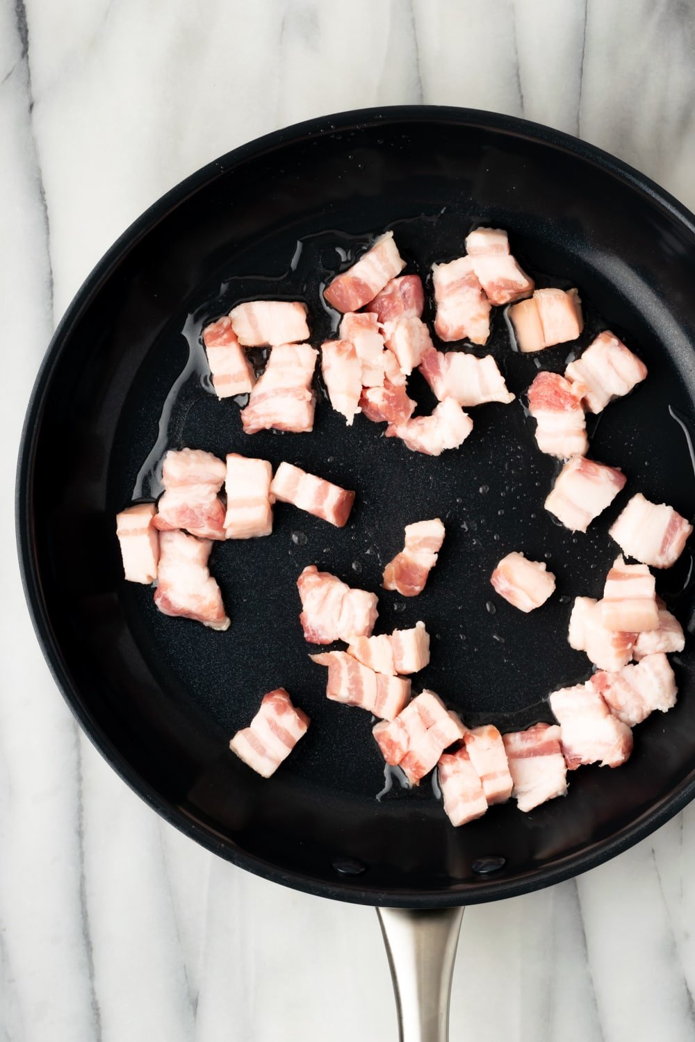 Uncooked pork belly pieces in a cast iron skillet on a marble background