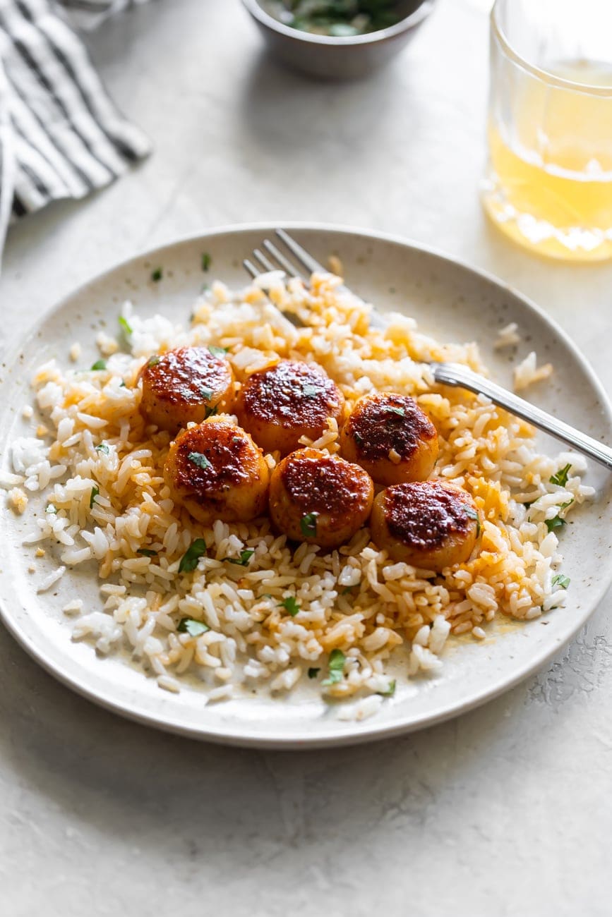 a white plate scallops tossed in spices with garlic butter served over white rice