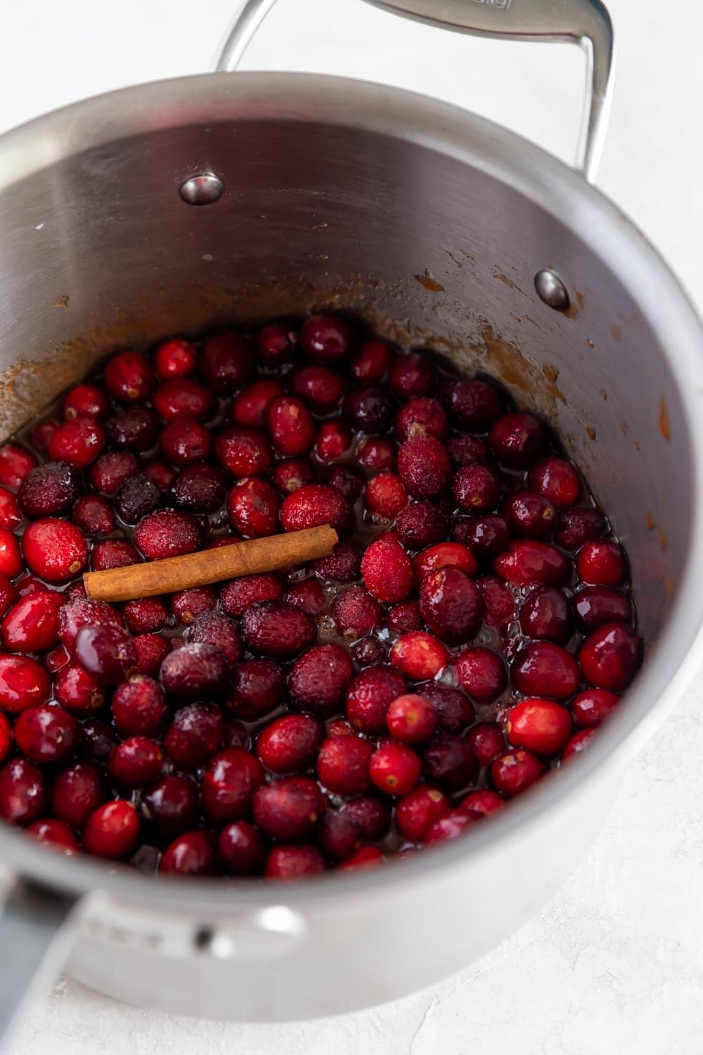 whole cranberries in a saucepan with a cinnamon stick on the stove