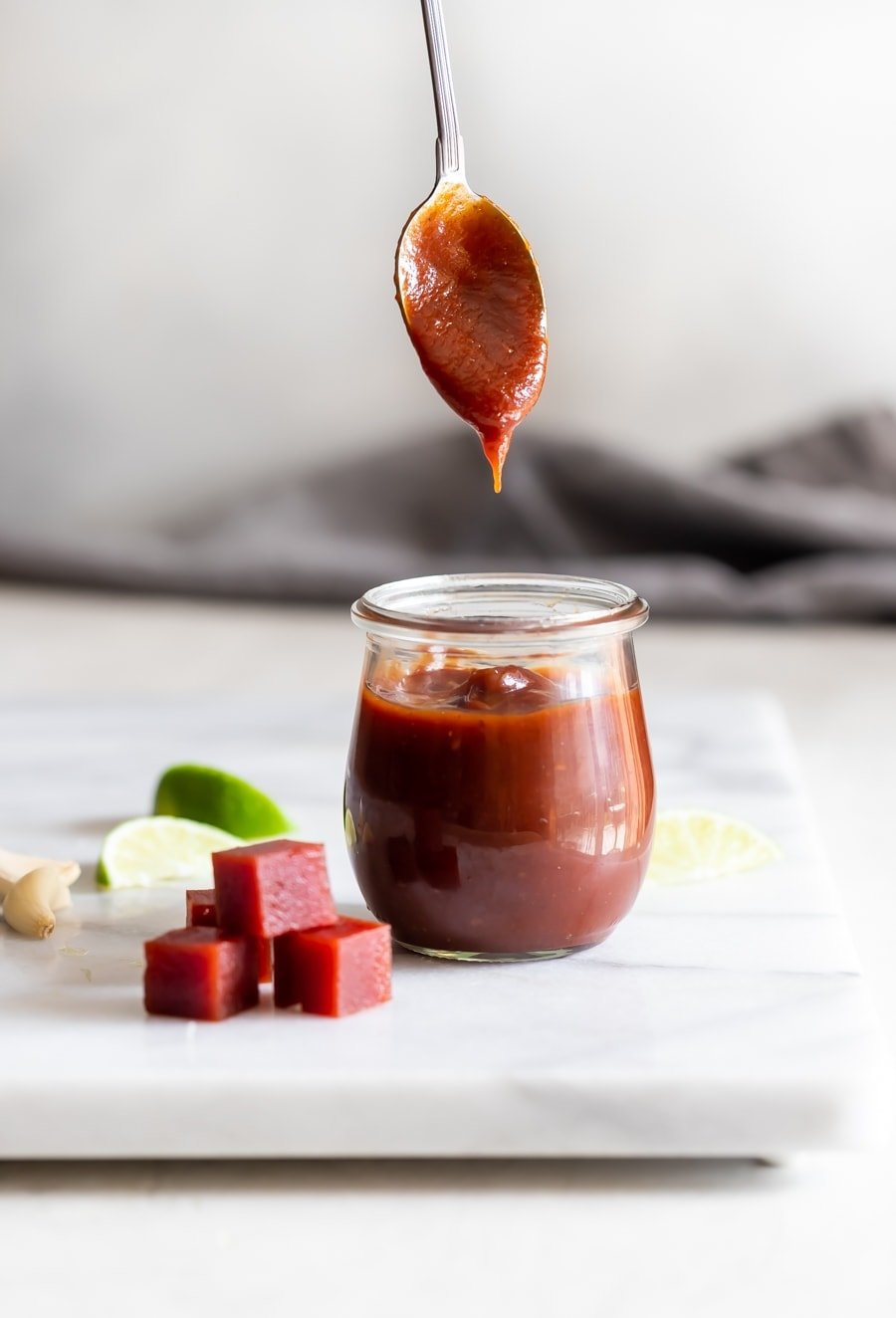 guava bbq sauce inside a weck jar with a spoonful of sauce on top with guava paste cubes on a marble slab