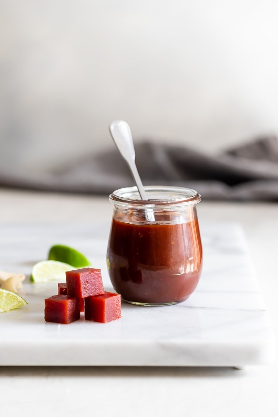 jar with guava bbq sauce and a silver spoon with guava paste cubes on a marble slab