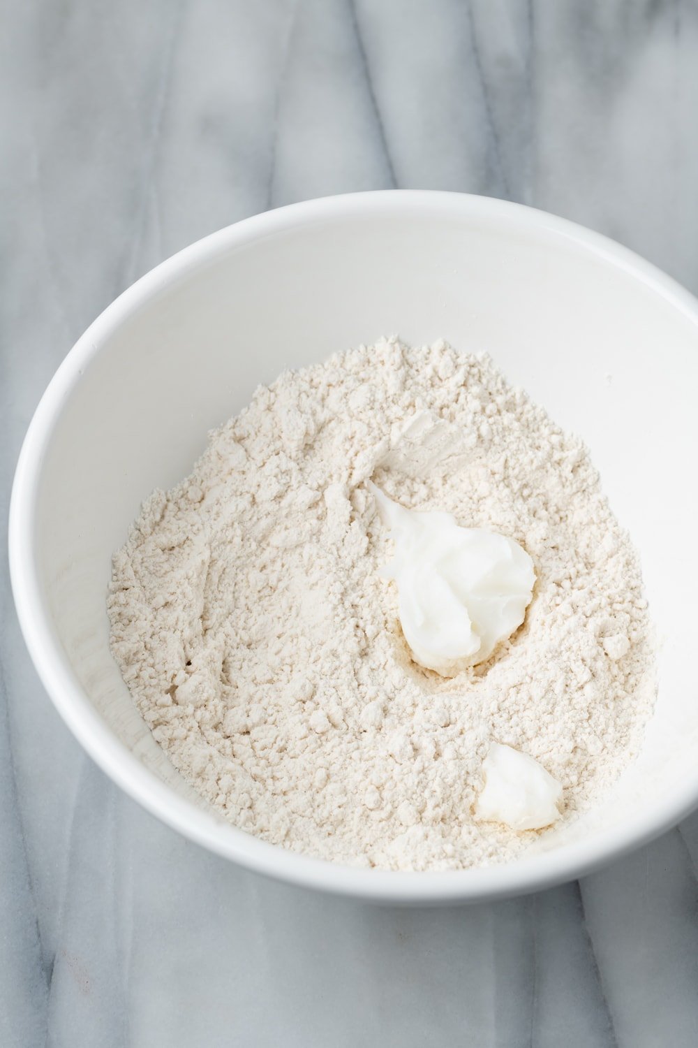 Flour, lard and salt in a white bowl before mixing for empanada dough