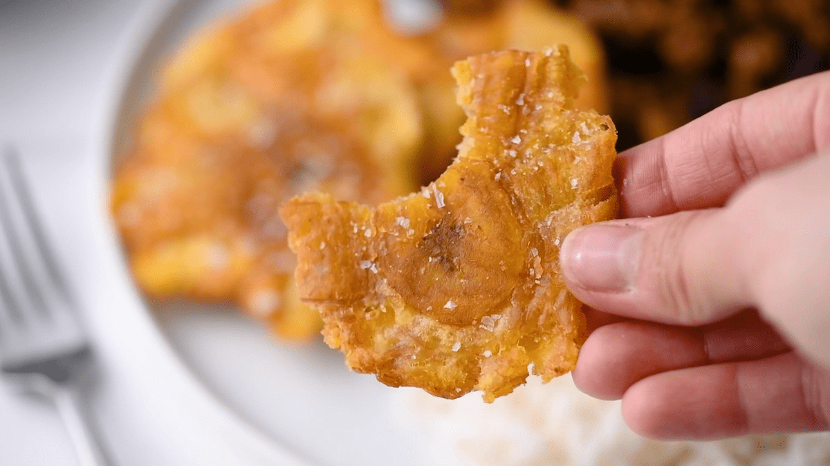 twice fried plantains (tostones) with salt being held by a hand