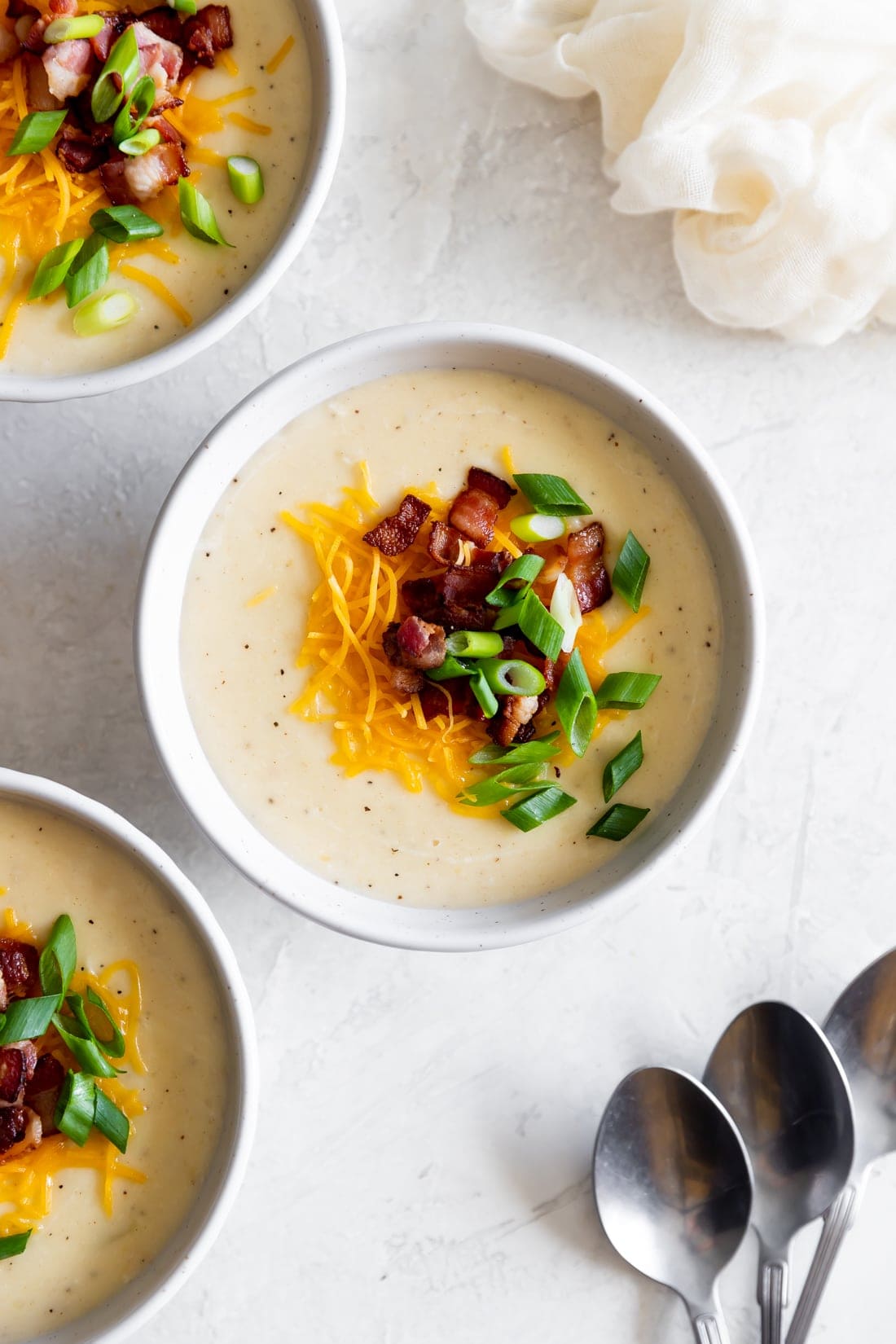 bowls of baked potato soup on a white background with silver spoons