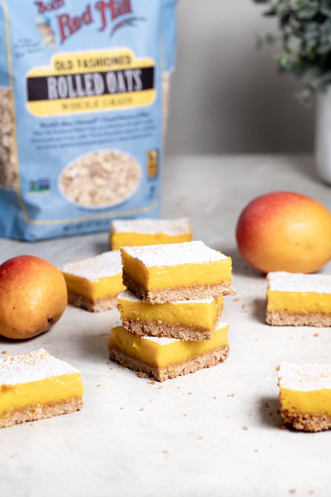 mango bars with shortbread crust made with oats and coconut flakes stacked on top of one another on a white table