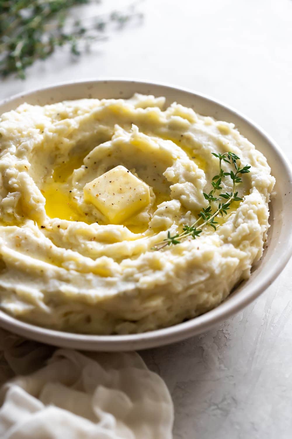 creamy mashed potatoes with butter in a ceramic bowl with thyme
