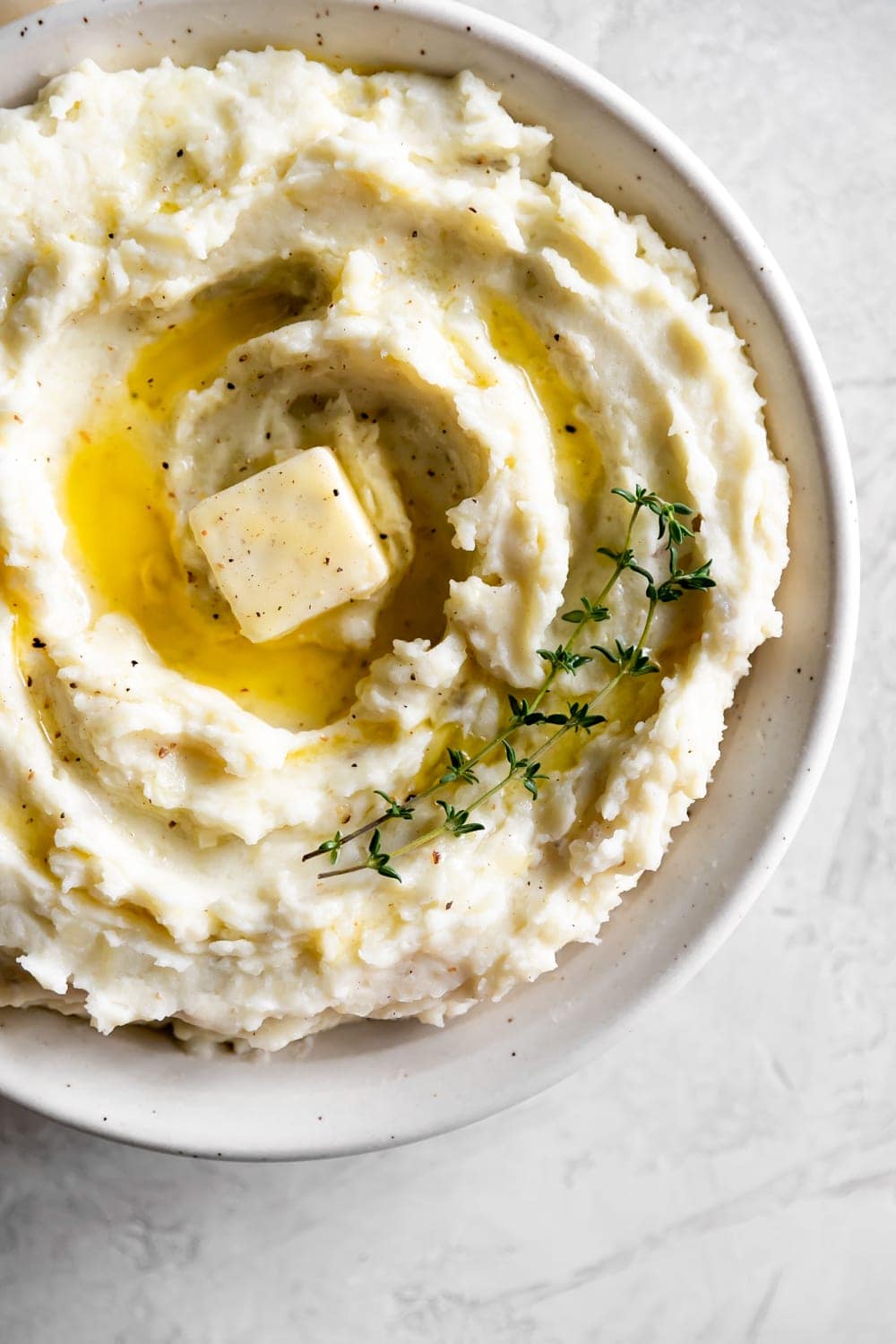 fluffy mashed potatoes with butter in a ceramic bowl with thyme
