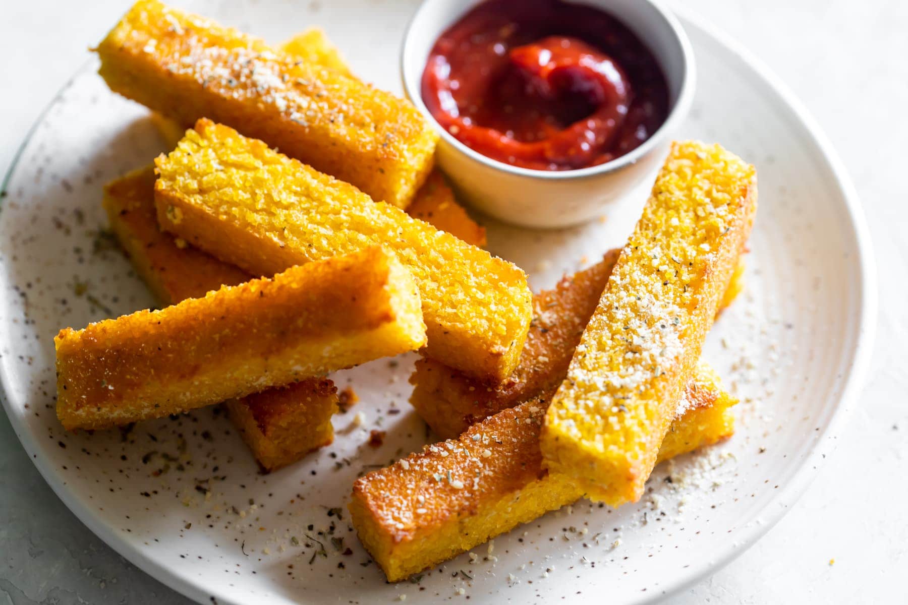 polenta fries on a white plate with grated parm on top