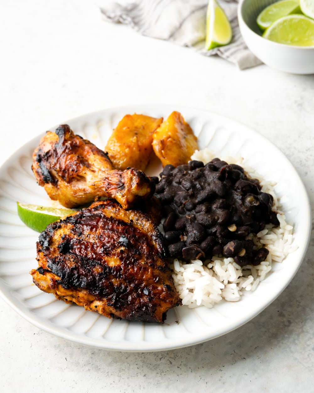 Cuban grilled chicken thighs with sweet plantains, rice and black beans on a white plate