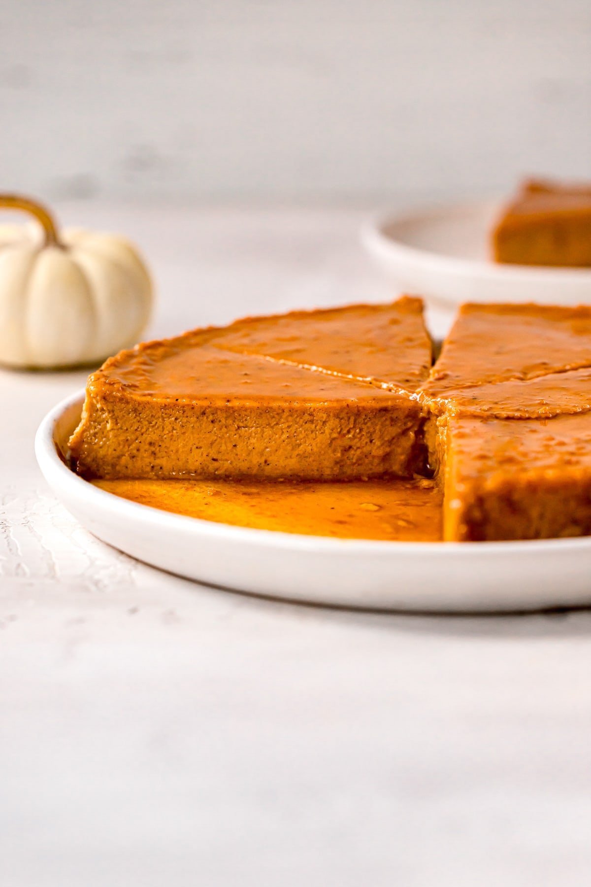 pumpkin flan slices on a white plate with caramel and decorative pumpkins